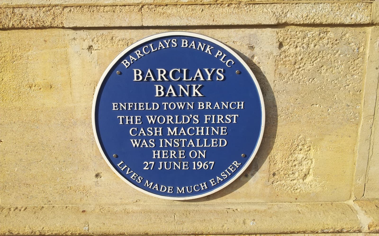 A round blue plaque on a stone wall reading Barclays Bank, Enfield Town Branch, the world's first cash machine was installed here on 27 June 1967