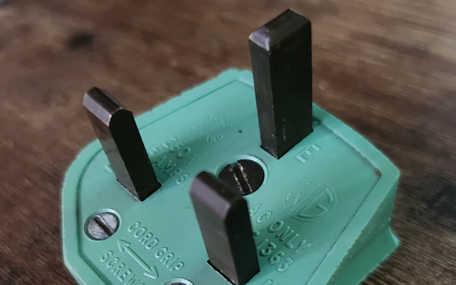 An old green British three-pin plug marked 13 amps and BS 1363, with three bare metal rectangular pins
