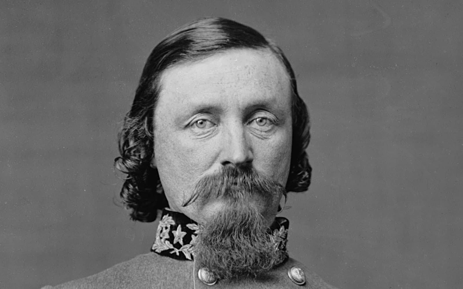 Black-and-white photograph of a man with long wavy hair, a drooping moustache and a pointed beard, in a military uniform with an embroidered collar