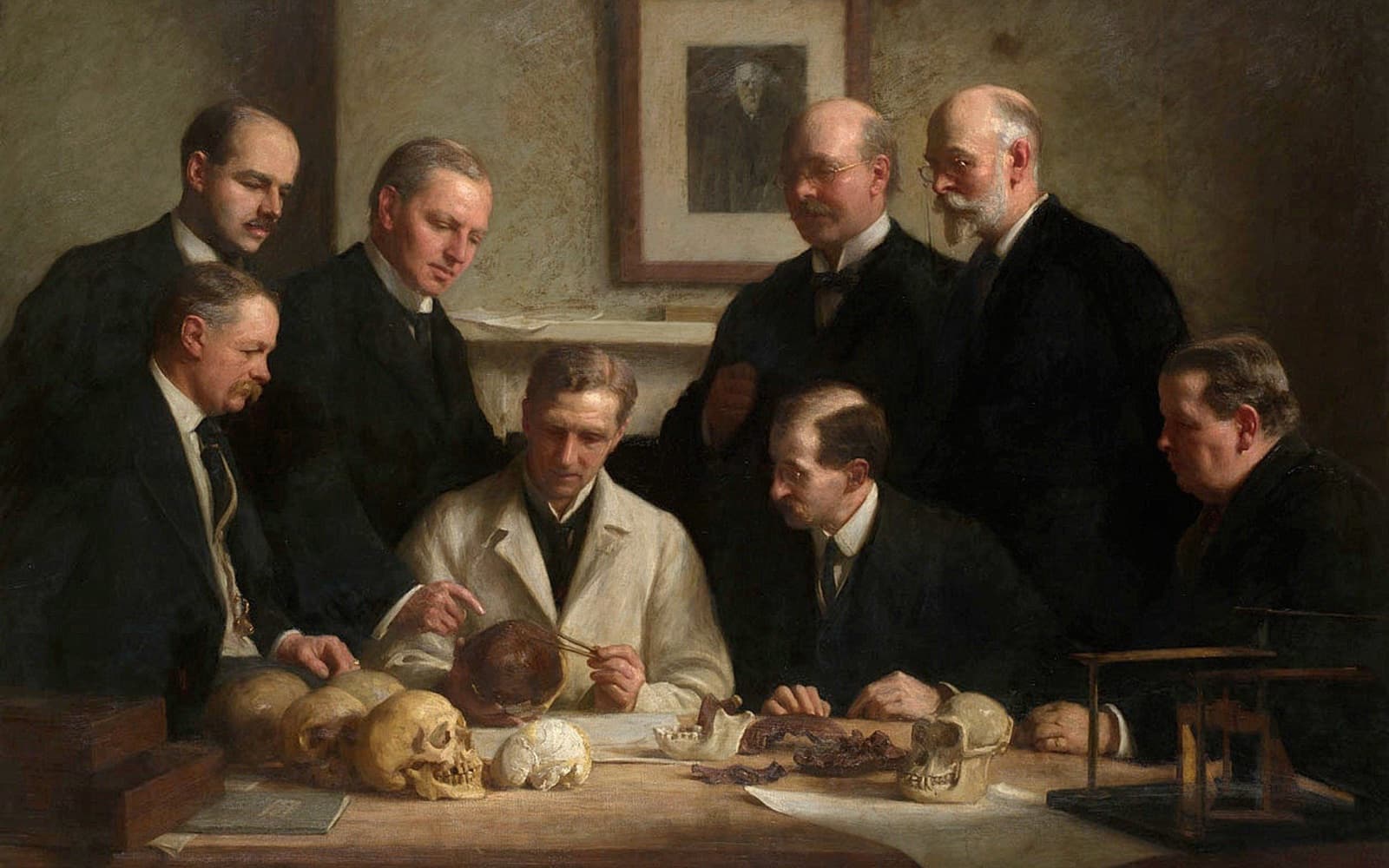 Painting of eight men, most in dark suits, gathered around a table examining a skull, with a portrait of Charles Darwin on the wall behind them