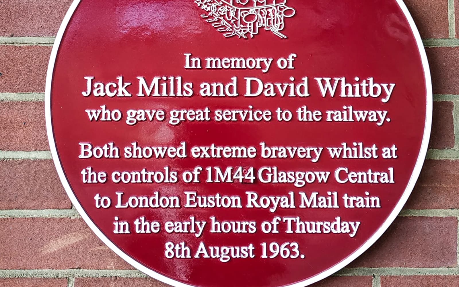 A round red plaque on a brick wall in memory of Jack Mills and David Whitby