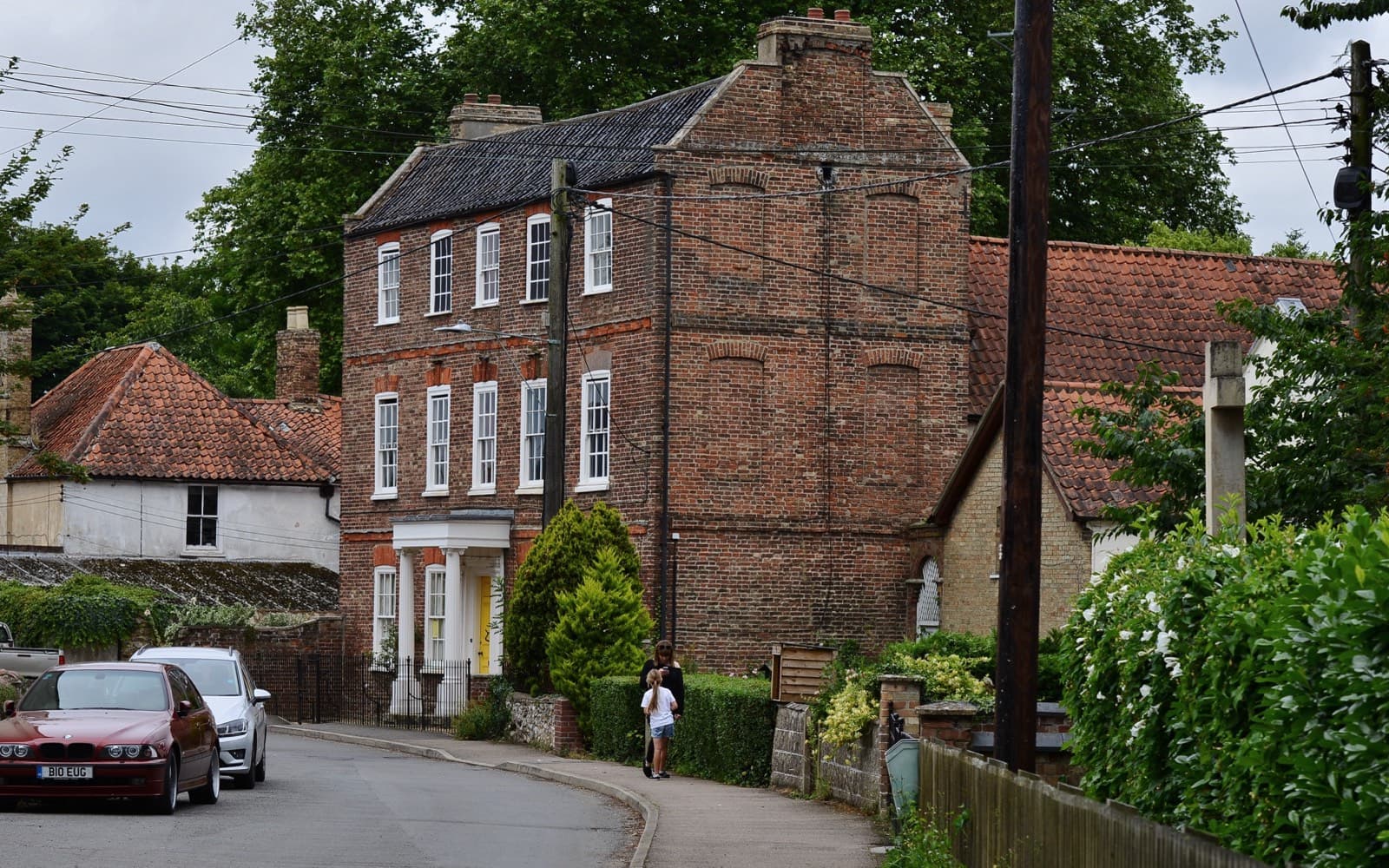 A tall red-brick Georgian house on a village street, its side wall marked with outlines of brick-filled window recesses