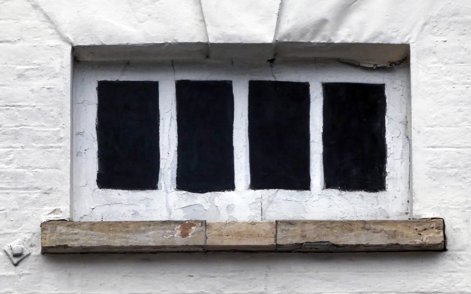 A blind window on a white-painted wall, with four black-painted panels framed in white to look like glass, above a stone sill