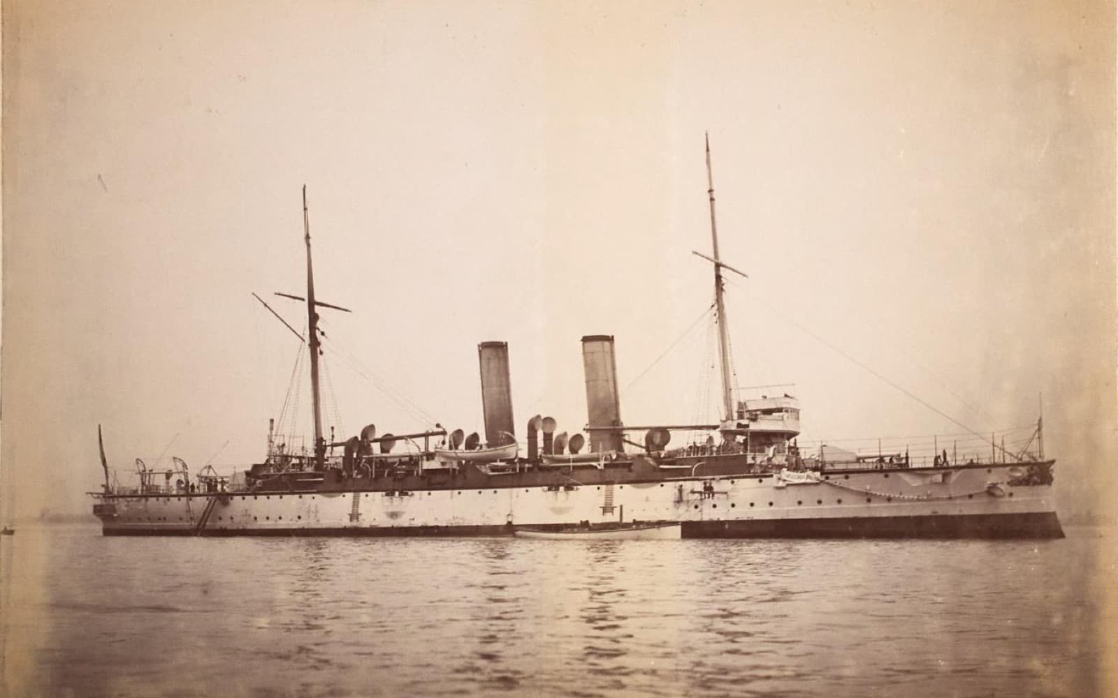 Old photograph of a large steam warship with two funnels and two masts, anchored on calm water
